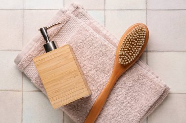 Masaj fırçası, bir şişe kozmetik ürün ve bej fayanslı havlu.