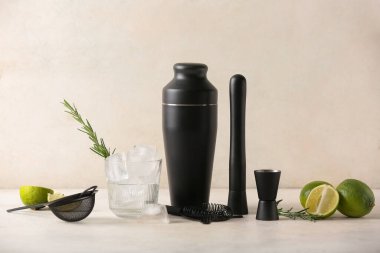 Farklı barmen aletleri, limon kokteyli bardakları ve bej rengi grunge arka planda malzemeler.