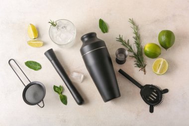 Farklı barmen aletleri, limon kokteyli bardakları ve bej rengi grunge arka planda malzemeler.