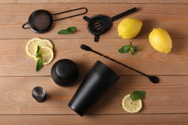 Ahşap arka planda farklı barmen aletleri ve kokteyl malzemeleri var.