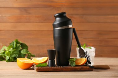 Farklı barmen aletleri, bardakta kokteyl ve ahşap arka planda malzemeler.