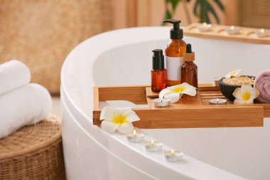 Küvet tepsisi, tesisat çiçekleri, kozmetik ürünleri şişeleri ve banyoda yanan mumlar, yakın çekim.