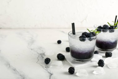 Lezzetli böğürtlenli bardaklar mermer masada, beyaz duvarın yanında, yakın plan.