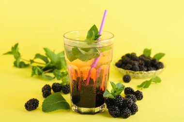 Lezzetli böğürtlenli limonata ve sarı arka planda malzemeler, yakın plan.