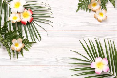 Güzel tesisat çiçeklerinden yapılmış çerçeve ve beyaz ahşap arka planda tropikal yapraklar