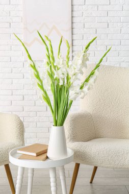 Güzel beyaz gladiolus çiçekleri ve kitaplarla dolu vazo oturma odasının iç tarafında, yakın plan.