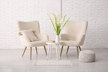 Rahat koltuklar, masa ve vazo. Oturma odasının içinde güzel beyaz gladiolus çiçekleri var.