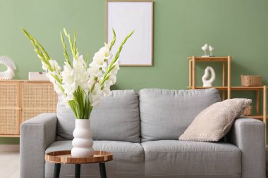 Gri rahat kanepe, masa ve vazo, oturma odasında güzel beyaz gladiolus çiçekleri, yakın plan.