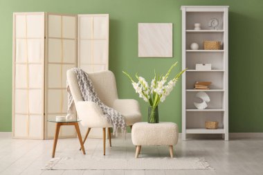 Koltuk, puf, masa ve vazo. Oturma odasının iç tarafındaki yeşil duvarın yanında güzel beyaz gladiolus çiçekleri.