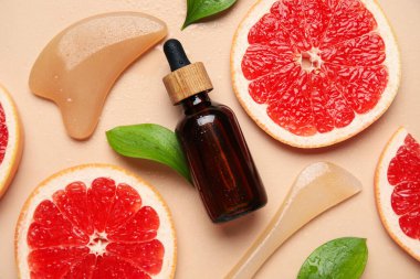Kozmetik ürün şişesi, yüz masajı aletleri ve bej arka planda bir dilim greyfurt, yakın plan.