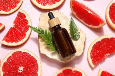 Bir şişe kozmetik ürünü, pembe arka planda greyfurt ve taş dilimleri, yakın plan.