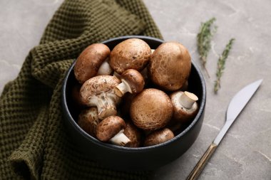 Gri grunge arka planda ham şampiyon mantarlı siyah kase, yakın plan.