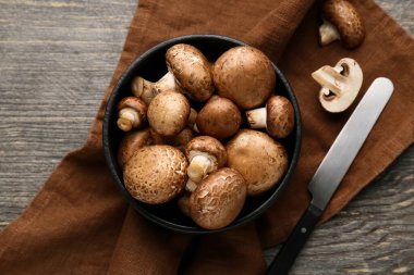 Gri ahşap arka planda çiğ şampiyon mantarlı peçete, bıçak ve kase yakın plan.