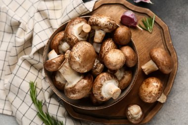 Tepsi, çiğ şampiyon mantarlı kase ve gri grunge arka planda peçete, yakın plan.