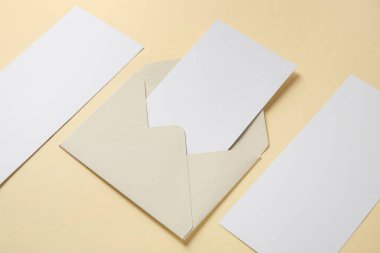 Bej arkaplanda boş kartlar ve zarf içeren kompozisyon, yakın plan