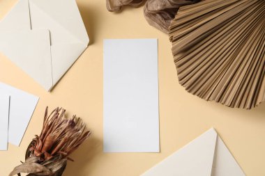Boş kart, zarf, kurutulmuş çiçek ve bej arka planda tropikal yaprak ile kompozisyon, yakın plan