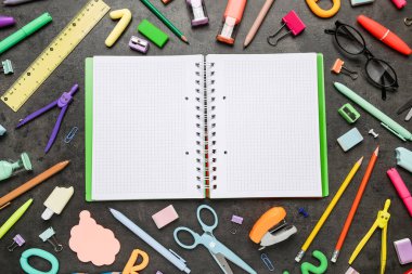 Boş bir defter, gözlük ve siyah grunge arka planında farklı okul malzemeleri, yakın plan.