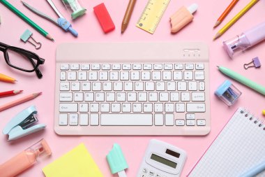 Gözlük, bilgisayar klavyesi ve pembe arka planda farklı okul malzemeleri, yakın plan.