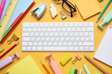 Gözlük, bilgisayar klavyesi ve turuncu arka planda farklı okul malzemeleri, yakın plan.