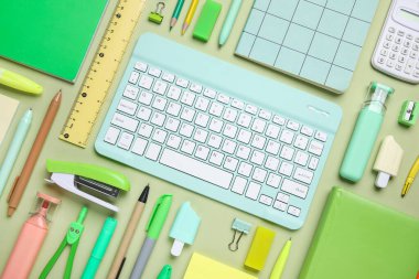 Yeşil arka planda bilgisayar klavyesi ve farklı okul malzemeleri, yakın plan