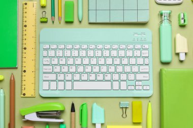 Yeşil arka planda bilgisayar klavyesi ve farklı okul malzemeleri, yakın plan