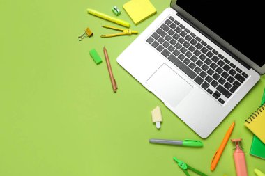 Modern dizüstü bilgisayarlı kompozisyon ve yeşil arka planda okul malzemeleri.