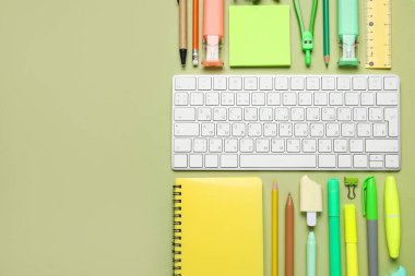 Yeşil arka planda bilgisayar klavyesi ve farklı okul malzemeleriyle kompozisyon, yakın plan