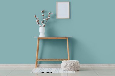 Oturma odasının içindeki yeşil duvarın yanında pamuk çiçekli vazo, masa ve vazo.