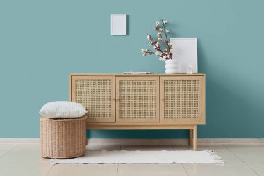 Pouf, çekmece ve vazo, oturma odasının iç tarafındaki yeşil duvarın yanında pamuk çiçekleri.