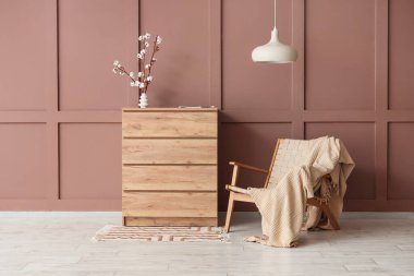 Hasır koltuk, çekmeceler ve vazo, oturma odasının iç tarafındaki kahverengi duvarın yanında pamuk çiçekler.