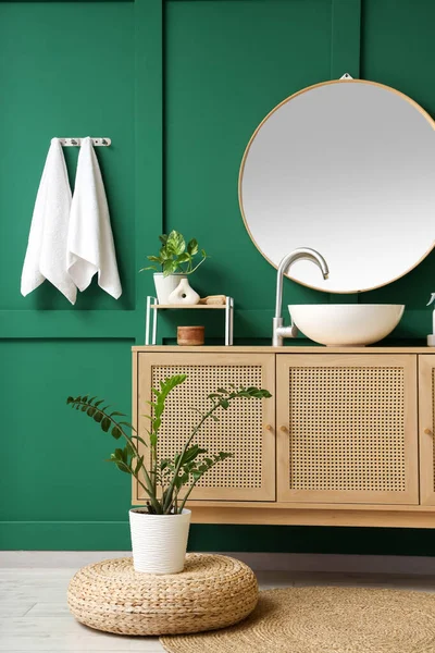 Modern lavabo, dolap ve bitkiler banyonun içindeki yeşil duvarın yanında.