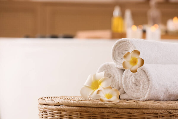 Plumeria цветы и чистые полотенца на плетеном столе в интерьере ванной комнаты, крупным планом
