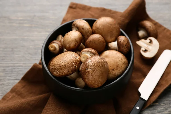 Gri ahşap arka planda çiğ şampiyon mantarlı peçete, bıçak ve kase yakın plan.