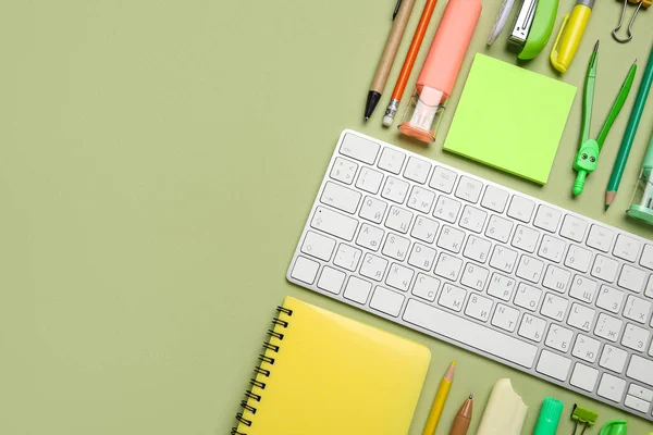 Yeşil arka planda bilgisayar klavyesi ve farklı okul malzemeleriyle kompozisyon, yakın plan