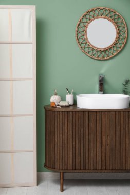 Banyoda yeşil duvarın yanında banyo malzemeleri olan modern lavabo.