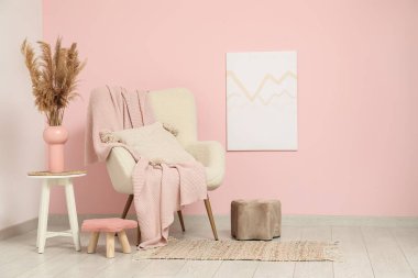 Yastıklı koltuk, ekose, puf ve pampa otlu vazo pembe duvarın yanında.