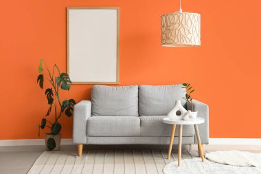 Gri kanepesi, kahve masası ve turuncu duvarın yanında bitkileri olan şık bir oturma odası.