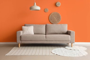 Turuncu duvarın yanında rahat gri kanepeli şık bir oturma odası.