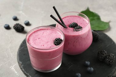 Gri arkaplanda taze böğürtlen suyu ve yabanmersini bardakları