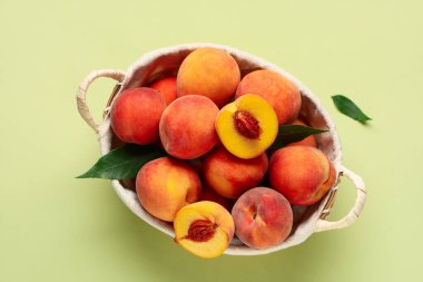 Yeşil arka planda tatlı olgun şeftalili hasır sepet.