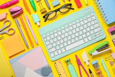 Modern bilgisayar klavyesine sahip kompozisyon, farklı kırtasiye malzemeleri ve sarı arka planda gözlük