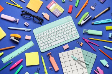 Modern bilgisayar klavyesi, gözlük ve mavi zemin üzerinde farklı kırtasiye malzemesi olan kompozisyon