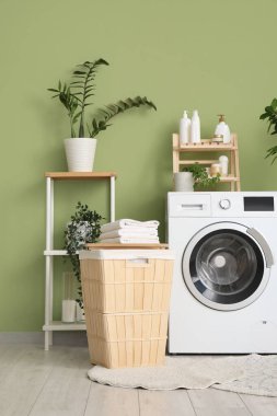 Çamaşır sepetinin, çamaşır makinesinin ve ev bitkilerinin olduğu odanın içi.