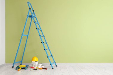 Yeşil duvarın yanında boya ve aletlerle dolu merdiven.