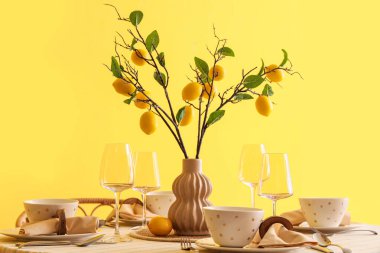 Yemek odasındaki sarı duvarın yanında güzel limon dallarıyla süslenmiş şık bir masa.