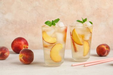 Şeftali dilimli bardaklar, buz küpleri ve bej duvarlı beyaz masa üzerindeki nane yaprakları.