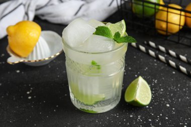 Limon dilimli bir bardak içki, buz küpleri ve siyah grunge arka planda nane yaprakları.