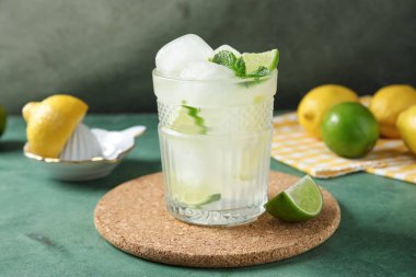 Yeşil grunge arka planda limon dilimleri, buz küpleri ve nane yapraklı bir bardak içki.