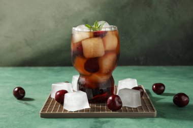 Bir bardak kirazlı içecek, buz küpleri ve yeşil grunge arka planda nane yaprakları.