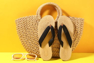 Sarı arka planda şık hasır plaj ayakkabıları, çanta ve güneş gözlükleri, yakın plan.